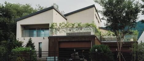 A modern two-story house with a garage, surrounded by a stone wall and greenery.