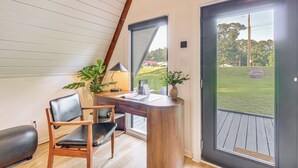 A modern room with a curved desk, a chair, a lamp, and a view of a grassy area through a large door. - Hot Tub, Grill & Fire Pit: Quiet Georgetown Escape (Savannah)