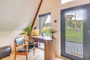 A modern room with a curved desk, a chair, a lamp, and a view of a grassy area through a large door. - Hot Tub, Grill & Fire Pit: Quiet Georgetown Escape (Savannah)