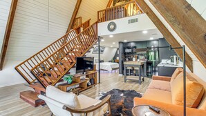 A loft-style living space with a wooden staircase, a kitchen area, a sofa, and a television. - Hot Tub, Grill & Fire Pit: Quiet Georgetown Escape (Savannah)