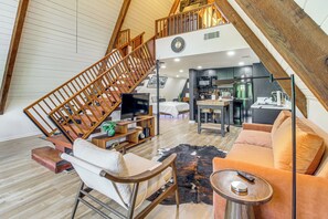 A loft-style living space with a wooden staircase, a kitchen area, a sofa, and a television. - Hot Tub, Grill & Fire Pit: Quiet Georgetown Escape (Savannah)