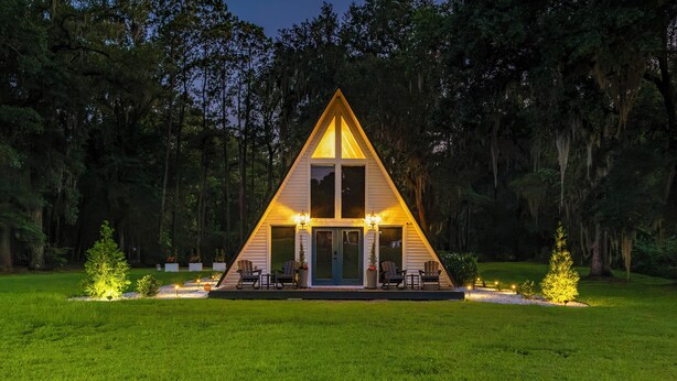 A triangular-shaped cabin with a porch, surrounded by a grassy area and trees. - Hot Tub, Grill & Fire Pit: Quiet Georgetown Escape (Savannah)