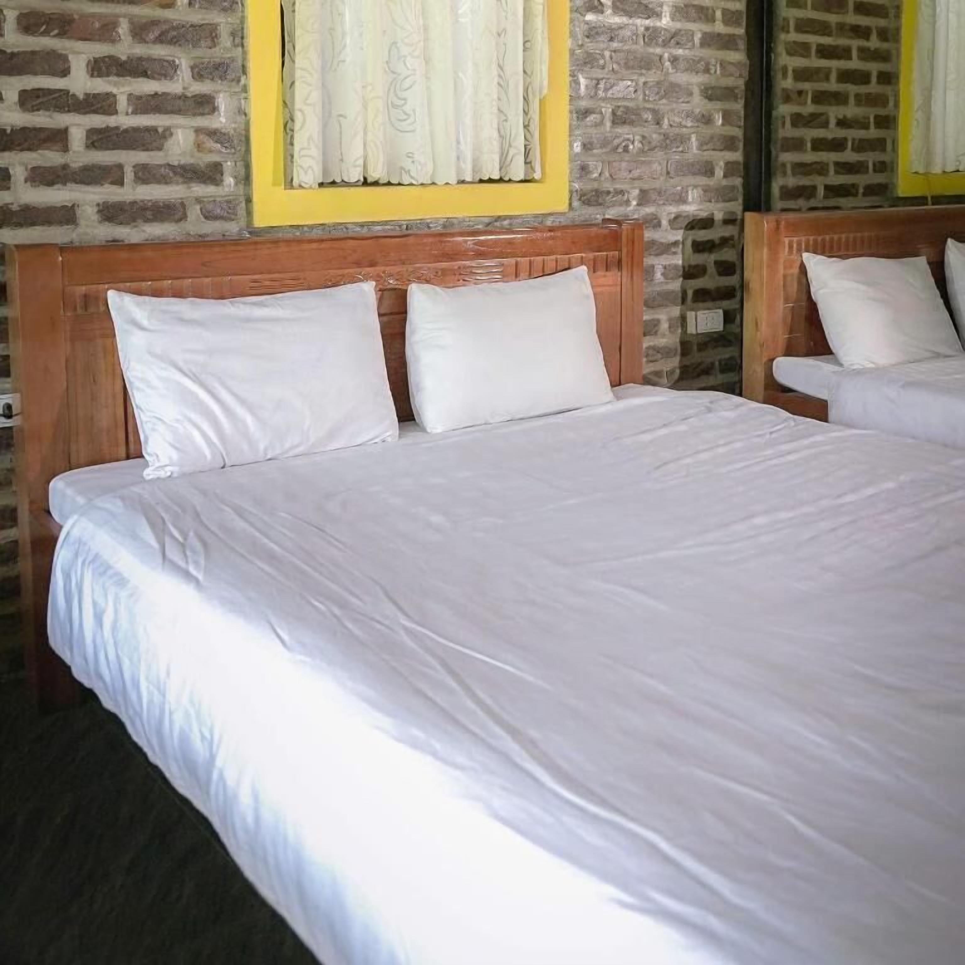 A hotel room with a brick wall, a wooden headboard, and a bed with white bedding.