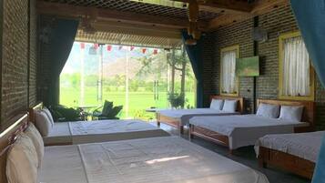 A room with four beds, a wooden ceiling, and a view of greenery outside.