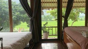 Ein Zimmer mit einem Bett, einem Sessel, einer Topfpflanze und Blick auf eine grüne Landschaft.