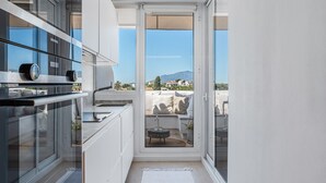 A modern kitchen with a Siemens oven, a dining area with a table and chairs, and a view of a balcony with a sofa and a mountain in the background. - Apartment 'Alexy' with Sea Views, Wi-Fi, and Air Conditioning (Marbella)