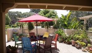 Een terras buiten met een tafel, stoelen en een rode parasol.
