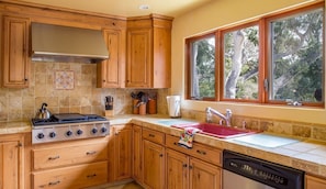 A kitchen with wooden cabinets, a gas stove, a dishwasher, and a window with a view of trees. - Mi Casa - Monterey Home - Del Monte Golf Course Frontage (Monterey)