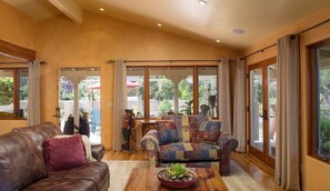 A spacious living area with a leather couch, patterned armchair, and a wooden coffee table. Large windows provide a view of the outdoors. - Mi Casa - Monterey Home - Del Monte Golf Course Frontage (Monterey)
