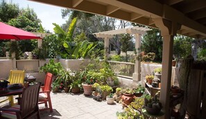 Een overdekt terras met een tafel en stoelen, omgeven door plantenbakken en een pergola.