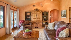 A living room with a brown leather sofa, a wooden coffee table with a plant, a leather armchair, and a wooden cabinet with shelves. - Mi Casa - Monterey Home - Del Monte Golf Course Frontage (Monterey)