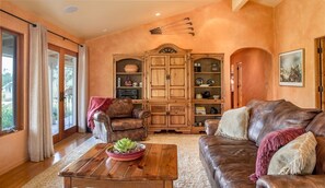 Ein Wohnzimmer mit einem braunen Ledersofa, einem Couchtisch aus Holz mit einer Pflanze, einem Ledersessel und einem Holzschrank mit Regalen.
