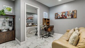 A modern living room with a sofa, a coffee table, and a desk with a chair. There is a bookshelf, a decorative plant, and a painting on the wall. - 5 Mi to Beach! Couple’s Apt w/ Yard in Port Richey (Port Richey)