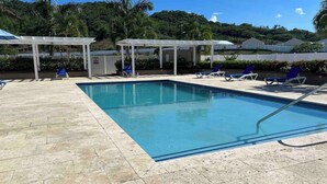 A rectangular swimming pool with clear blue water, surrounded by a tiled deck. There are lounge chairs and a covered seating area with a white roof. - Oceanpointe Serenity Get Away-solar Pool Wifi (Lucea)