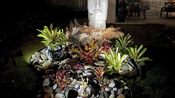Um jardim com uma escultura de pedra, diversas plantas e um caminho de pedra.