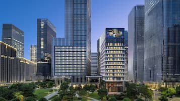 A modern hotel with a glass facade, surrounded by high-rise buildings and a well-maintained park area.