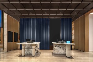A hotel lobby with two reception desks, a blue curtain backdrop, and a modern ceiling design. - Hampton by HiltonShenzhen NanshanQianhai (Shenzhen)