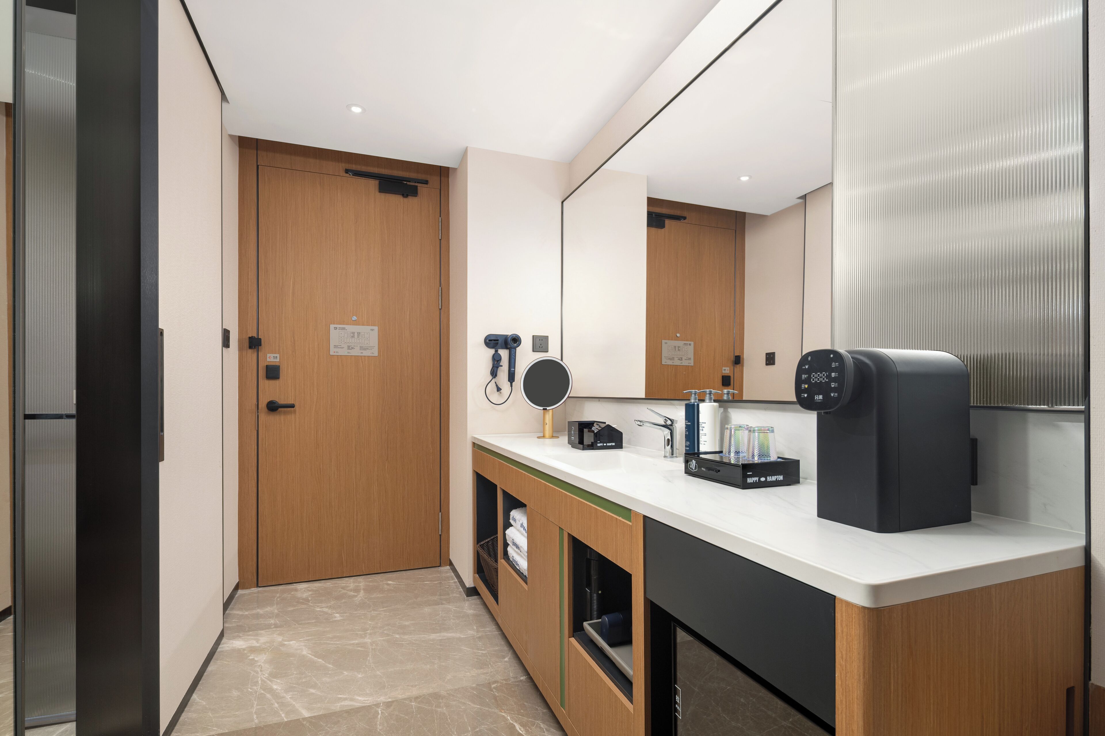 A modern bathroom with a wooden door, a sink with a mirror, a coffee machine, and toiletries.