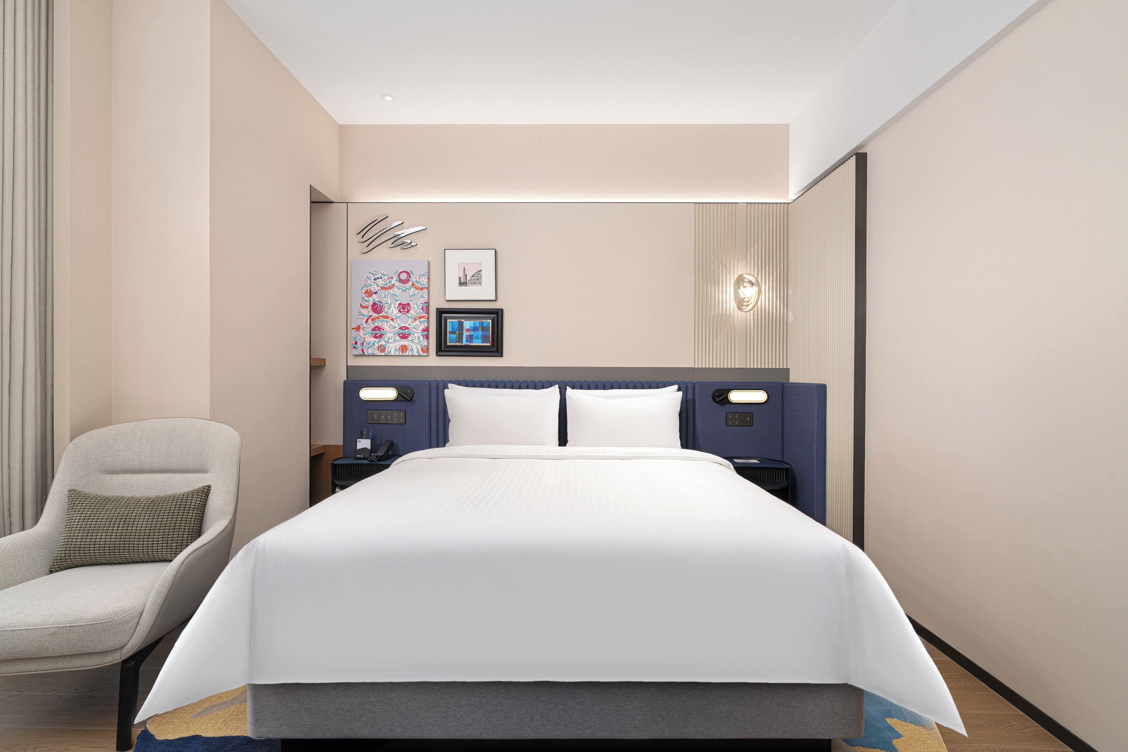 Une chambre d’hôtel avec un grand lit, une chaise, une table de chevet et des œuvres d’art accrochées au mur.