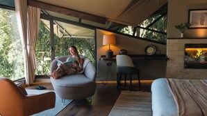 A modern room with a sofa, a chair, a bed, a fireplace, and a large window with curtains.