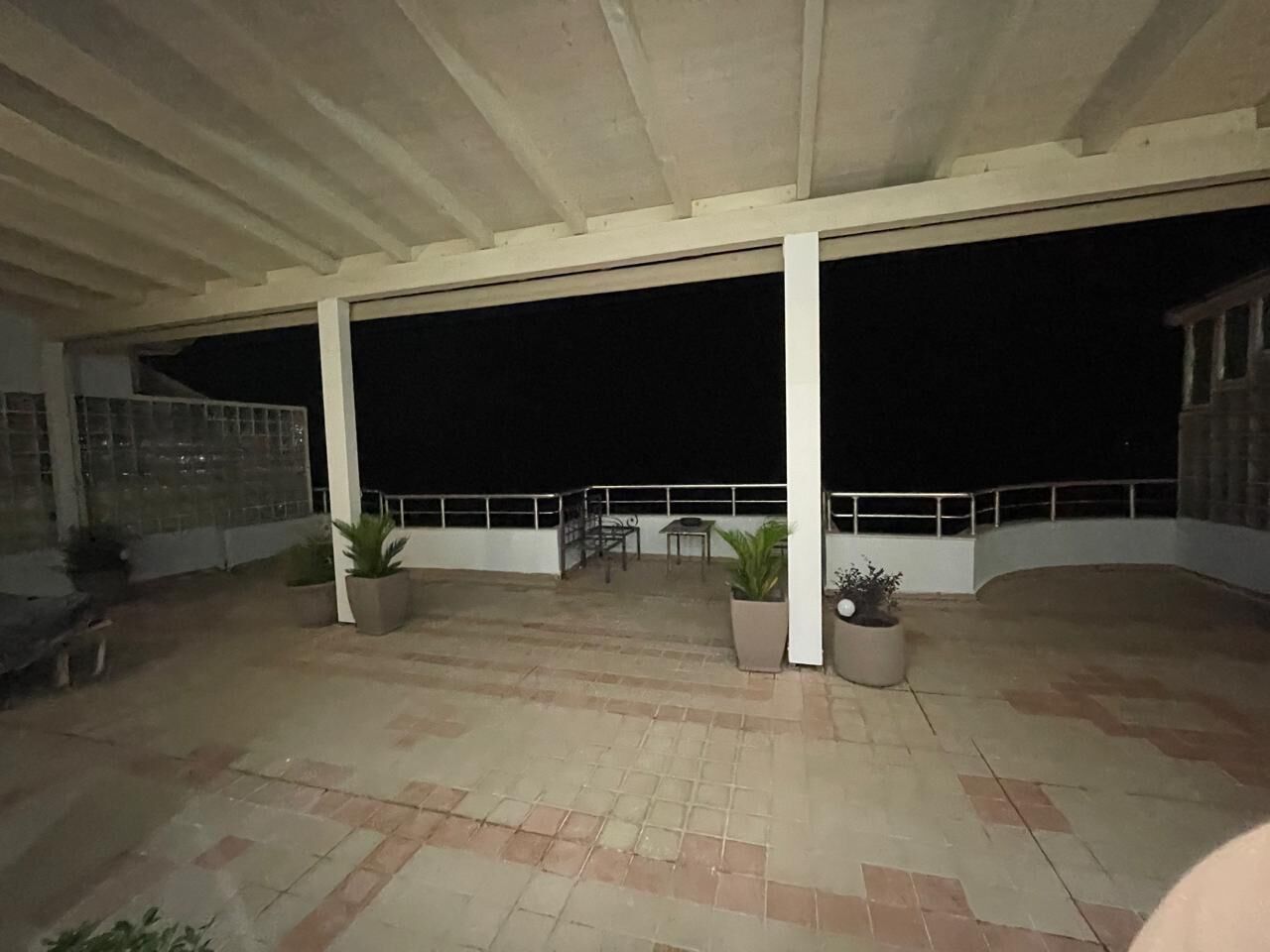 Un'area patio esterna coperta, con pavimento piastrellato, piante in vaso, un tavolo e sedie.