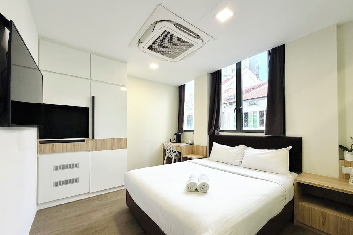 A hotel room with a bed, a desk, a chair, a TV, and a window with a view of buildings.