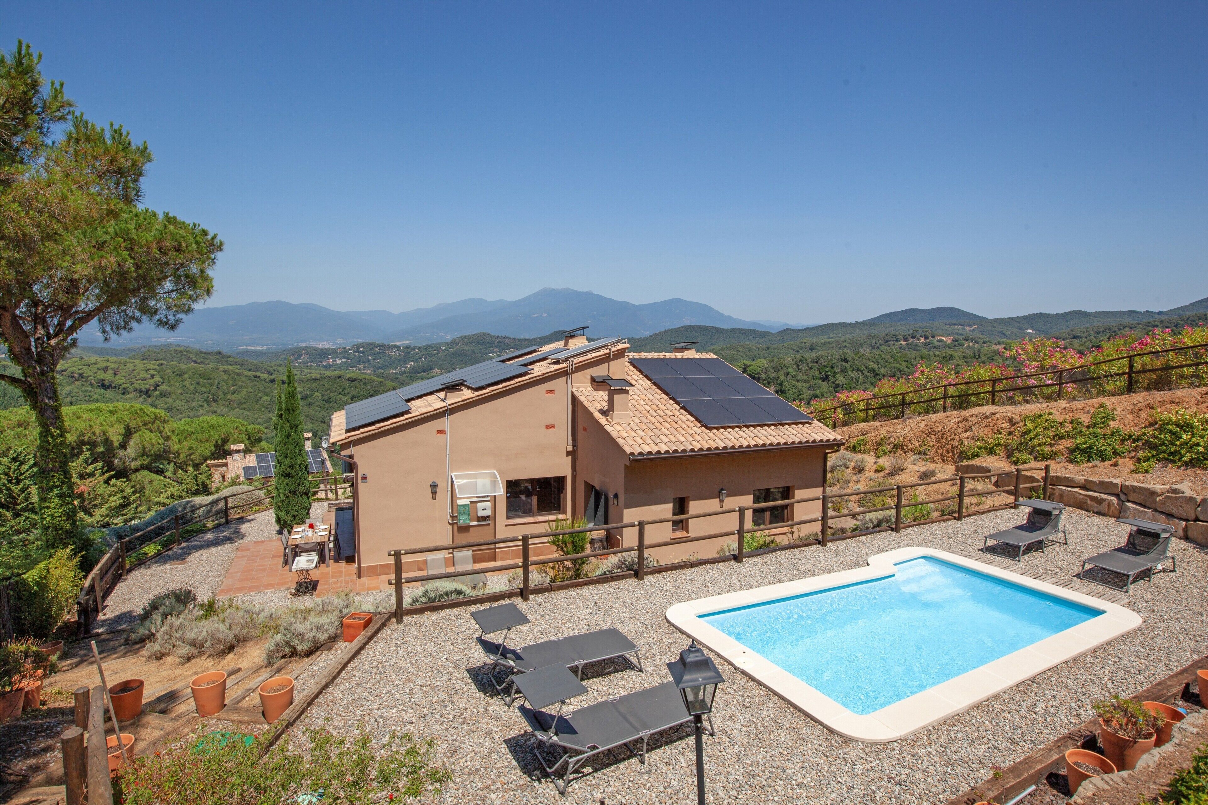 Una casa con piscina, paneles solares y vistas a las montañas.