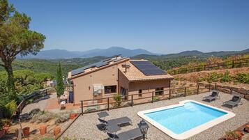 Una casa con piscina, paneles solares y vistas a las montañas.