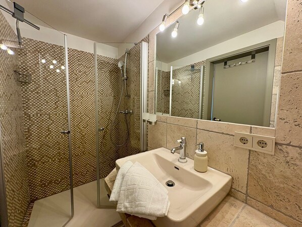 Une salle de bain avec une douche à parois de verre, un lavabo avec un miroir et un porte-serviettes.