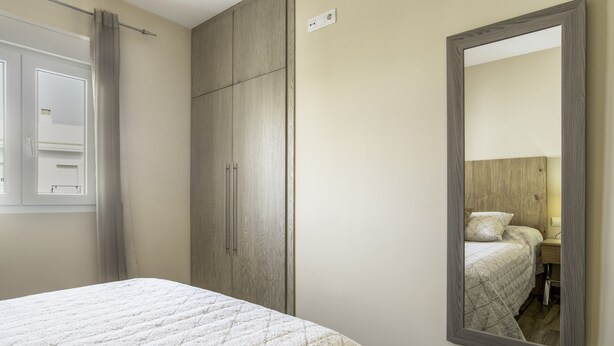 Een slaapkamer met een bed, een kledingkast, een spiegel en een raam met gordijnen.