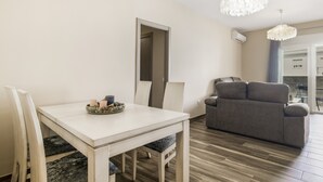 Een moderne woonkamer met een eethoek, een grijze bank en een kroonluchter.