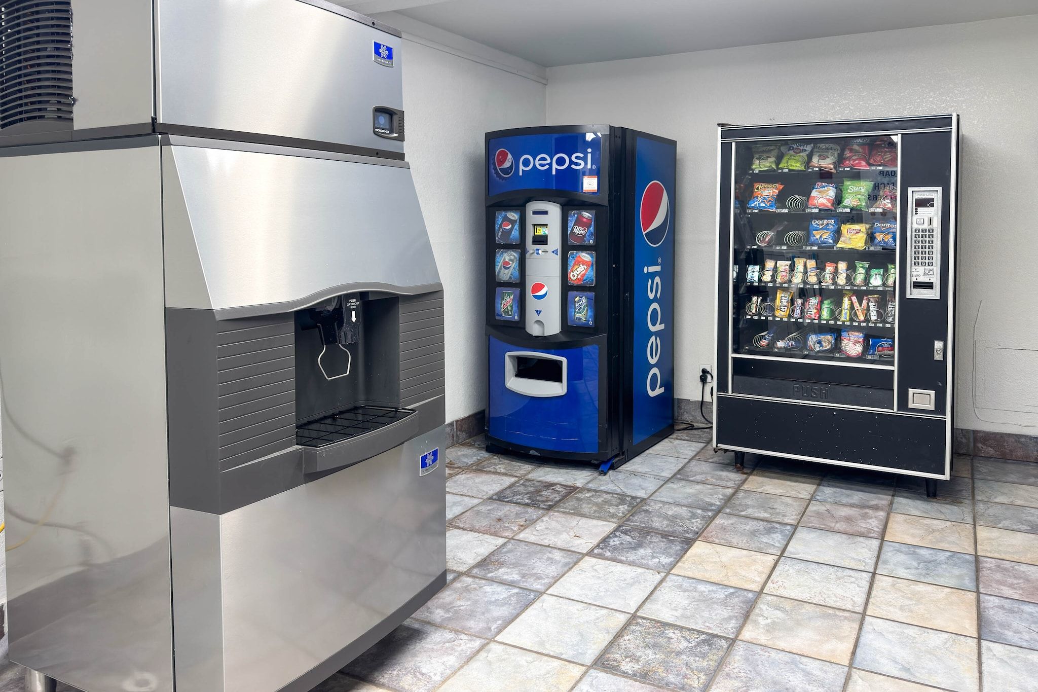Een professionele keuken met een roestvrijstalen koelkast, een Pepsi automaat en een koelvitrine.