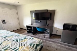 A bedroom with a bed, a desk, a chair, a television, and a refrigerator.