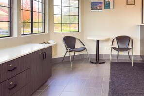 A reception area with a counter, two chairs, a small table, and a poster on the wall.