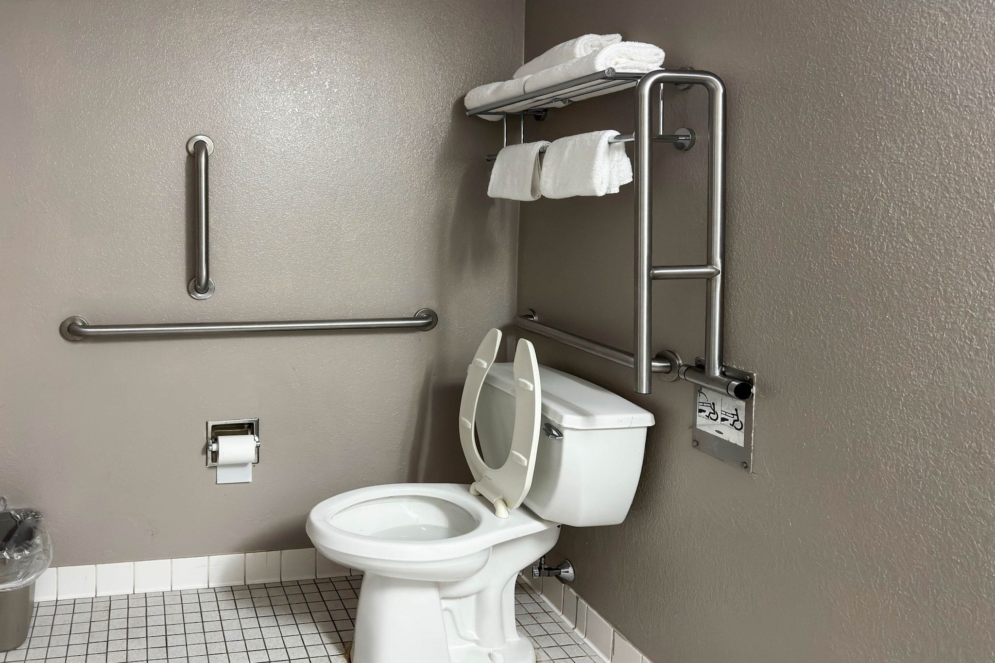 Ein Badezimmer mit Toilette, Haltegriff, Handtuchhalter und Toilettenpapierhalter.