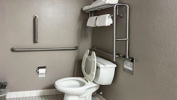Ein Badezimmer mit Toilette, Haltegriff, Handtuchhalter und Toilettenpapierhalter.