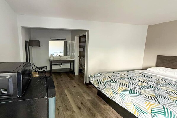 A hotel room with a bed, a desk with a chair, a mirror, and a television.