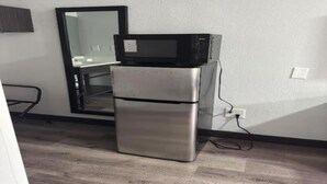 Una kitchenette compacta con microondas y refrigerador, un espejo y un enchufe en la pared.