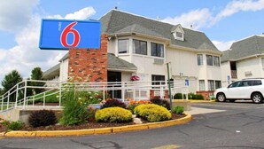 A motel with a prominent '6' sign, a brick entrance, and a parking lot with a white car. - 1 Full Bed|Mobility Access|Tub,Nsmk (Enfield)