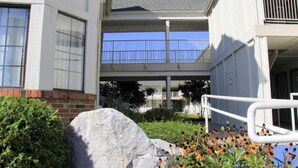 Un edificio de varios pisos con un paseo techado, una gran roca y plantas florecientes.