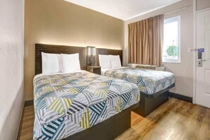 Ein Hotelzimmer mit zwei Betten, Holzboden, einem Fenster mit Vorhängen und einer Tür.