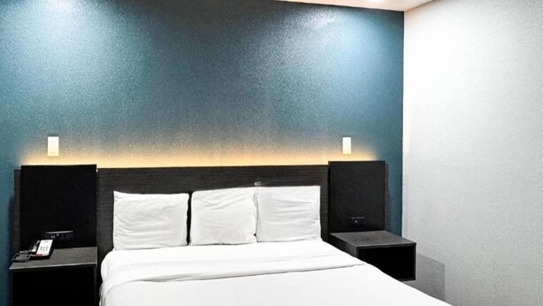 Habitación de hotel con una cama, dos mesitas de noche y una lámpara de pared.