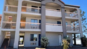 A multi-story building with balconies, a central entrance, and a landscaped area with rocks and plants.