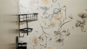 Une douche avec un papier peint à motifs floraux, une pomme de douche noire et un porte-serviettes noir.