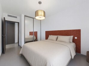 Una habitación de hotel moderna con cama, espejo, puerta y lámpara de techo.