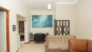 Un salon avec un canapé beige, une table à manger avec des chaises, une grande peinture abstraite et un élément de séparation décoratif.