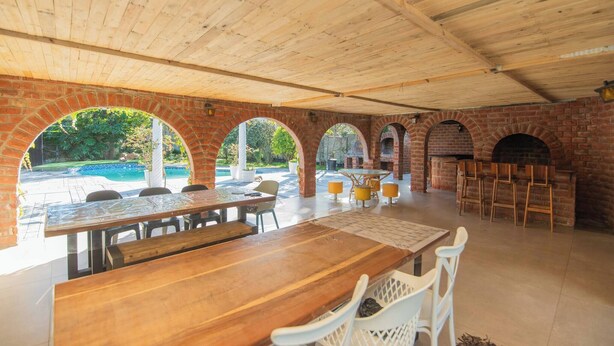 Un espace de restauration en plein air agrémenté d’arches en briques, de tables et de chaises en bois, et offrant une vue sur une piscine.