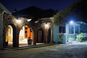 A stone archway leading to a building with a door, surrounded by potted plants and a well-lit area.
