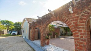 Un arc en briques mène à une maison dotée d’un garage, d’une allée gravillonnée et d’un pot de fleurs.