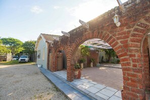 A brick archway leading to a house with a garage, a gravel driveway, and a potted plant.